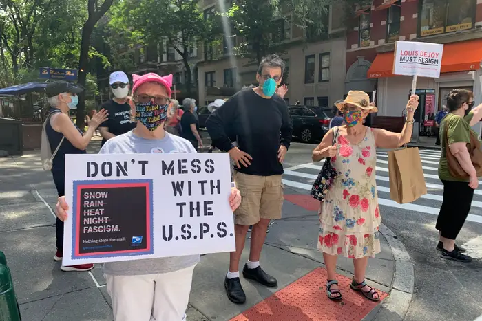 Protesters calling to ensure the U.S. Postal Service is meddled with hold up signs that read "Don't Mess With The U.S.P.S." and "DeJoy Must Resign."